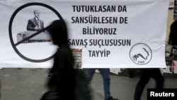 A woman walks past a banner picturing Turkish President Recep Tayyip Erdogan that reads, "When you arrest (journalists) or censor (media) we know that you are a war criminal, Tayyip," during a protest over the arrest of journalists in Turkey.