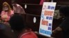 FILE - Activists wearing a rainbow mask sit at the Botswana High Court place placards as they listen to court proceeding, Oct. 12, 2021. 