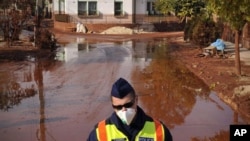 A Hungarian police officer wearing a protective mask guards a street covered by toxic red sludge in Devecser, Hungary, 13 Oct 2010