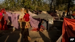 আফগানিস্তানের কাবুলে বাস্তুচ্যুত মানুষের একটি শিবিরে একজন মহিলা একটি শিশুকে কোলে নিয়ে দাঁড়িয়ে আছেন। সেপ্টেম্বর ১৩, ২০২১। 