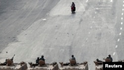 Two men on a scooter ride near soldiers on military vehicles at Abbasiya square near Egypt's Defence Ministry, in Cairo, May 4, 2012. 