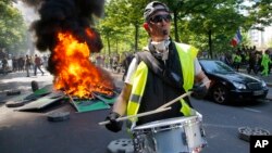 A man bangs a drum in front of a fire on the street during a yellow vest demonstration in Paris, Apr. 20, 2019. 