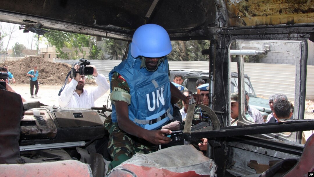 A U.N. observer takes pictures of a military bus that was damaged by a roadside bomb, at al-Bahdaliyah area, near Damascus, Syria, Wednesday, May 23, 2012. 