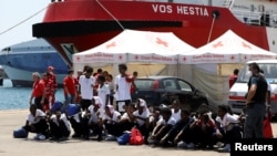 Migrants sit on the ground after disembarking from Vos Hestia ship of NGO "Save the Children" in the Sicilian harbour of Augusta, Italy, Aug. 4, 2017. 