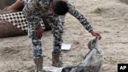 An Iraqi policeman peeks into a blanket containing a body found in a mass grave in Mosul containing some two dozen people, many of them children, in an area re-taken from Islamic State militants in Hamam al-Alil, Iraq, March 15, 2017. 