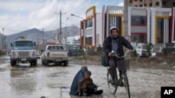 An Afghan man rides his bicycle past a woman and a boy sitting on a flooded street begging for money, following a heavy rain in Kabul, Afghanistan, April 2, 2014. 