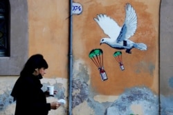 Una mujer pasa por un mural que presenta vacunas contra el covid lanzadas en paracaídas por una paloma blanca, pintado cerca del Ministerio de Salud, en Roma, el domingo 4 de abril de 2021.