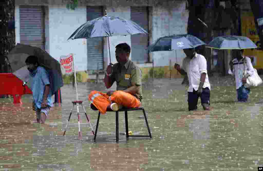 A local municipal worker sits on guard near an open manhole on a waterlogged street in Mumbai, India.