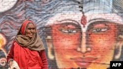 A Hindu pilgrim walks in front a mural of Hindu god Shiva after taking a holy dip in the sacred waters of Sangam, the confluence of Ganges, Yamuna and mythical Saraswati rivers, during the Maha Kumbh Mela festival in Prayagraj on January 13, 2025.