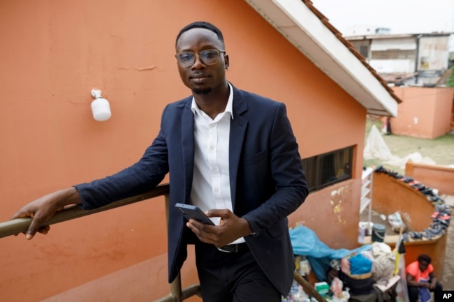 Shadrach Damateye, a co-founder of Masters Hive Center for Innovation, who uses his mobile phone to help business owners, poses for a photograph outside his office in Tema, Ghana, Tuesday, April 23, 2024. (AP Photo/Misper Apawu)