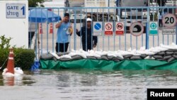 FILE - Workers look on behind flood protection barriers built at their factory at Amata Nakorn industrial Estate in Chonburi province, east of Bangkok, Oct. 9, 2013.