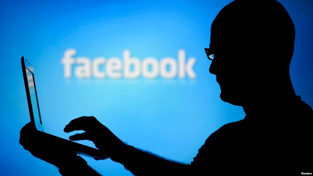 A man is silhouetted against a video screen with an Facebook logo as he poses with an Dell laptop in this photo illustration taken in the central Bosnian town of Zenica, August 14, 2013. REUTERS/Dado Ruvic 