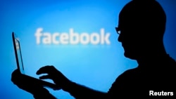 A man is silhouetted against a video screen with an Facebook logo as he poses with an Dell laptop in this photo illustration taken in the central Bosnian town of Zenica, August 14, 2013. REUTERS/Dado Ruvic 