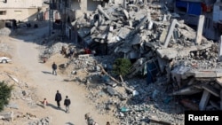 Palestinians ride a donkey-drawn cart as others walk past the rubble of houses, destroyed in previous Israeli strikes, amid the Israel-Hamas conflict, in Khan Younis, southern Gaza Strip