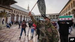 A masked fighter carries a flag of the Hayat Tahrir al-Sham group as others hold flags of the Syrian opposition, in the courtyard of the Umayyad Mosque in the old walled city of Damascus, Syria, Dec. 10, 2024.