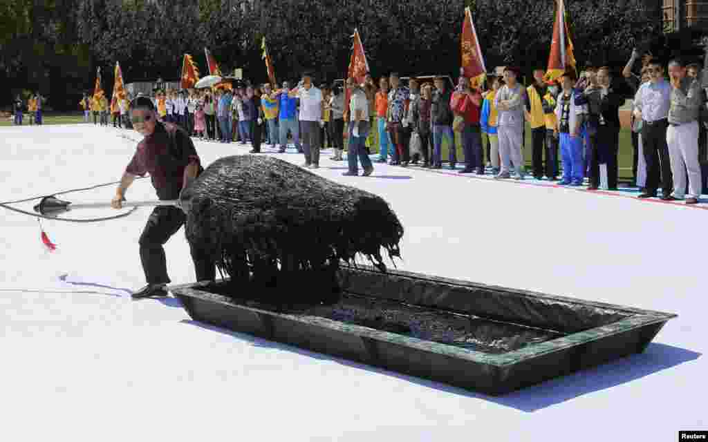 Calligrapher Zhang Kesi dips his brush with ink as he works on a giant calligraphy in Shenyang, Liaoning province, China. Zhang, best known for his giant Chinese calligraphy works written with oversized writing brushes, finished a new calligraphy. It will be presented as a gift to the upcoming National Games to be held in the city from Aug. 31 to Sept. 12.