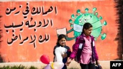 FILE - Children cross a street in front of a mural raising coronavirus awareness, in Syria's northeastern city of Qamishli, March 9, 2021.