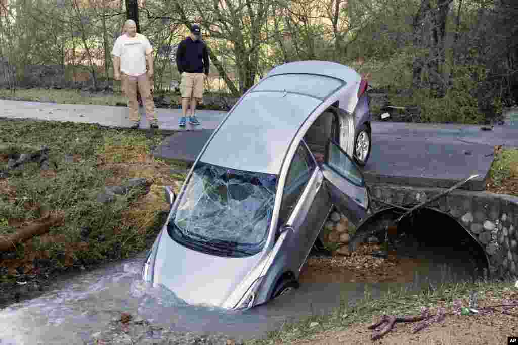 Tanager Tyler and son Mitchell look over a vehicle, Dec. 26, 2015, that wound up in the culvert of their driveway after floodwaters swept it and its four occupants off the road during the previous night, in Pinson, Alabama.&nbsp;The occupants had to be rescued by the fire department.