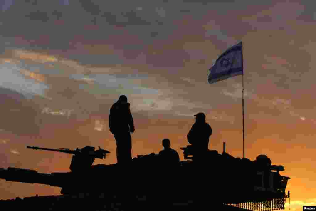 Tentara Israel berdiri di atas tank, bersiap meninggalkan perbatasan Gaza pada saat matahari terbit (22/1).