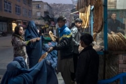 FILE - A man disributes bread to women outside a bakery in Kabul, Afghanistan, Dec, 2, 2021.