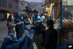FILE - A man disributes bread to women outside a bakery in Kabul, Afghanistan, Dec, 2, 2021.