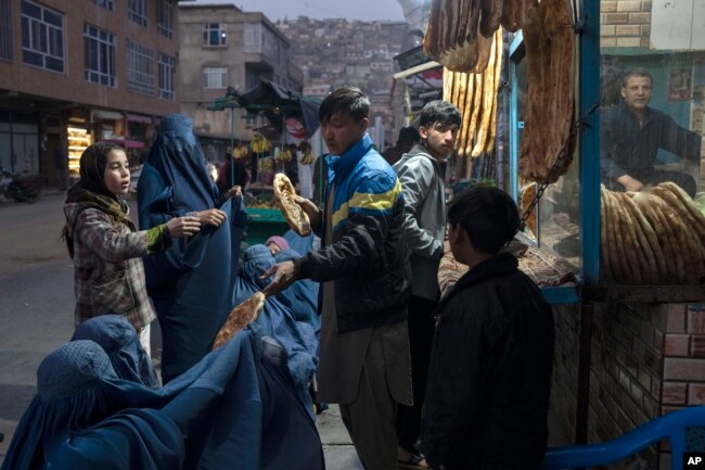 FILE - A man disributes bread to women outside a bakery in Kabul, Afghanistan, Dec, 2, 2021.