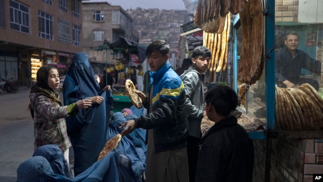 FILE - A man disributes bread to women outside a bakery in Kabul, Afghanistan, Dec, 2, 2021.