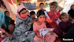 Seorang perempuan pengungsi membantu seorang gadis mengenakan masker yang dibagikan oleh UNICEF, di sebuah kamp darurat, di tengah pandemi COVID-19 di Jalalabad, Afghanistan 22 Juni 2020. (REUTERS/Parwiz/File Foto)