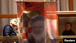 Bosnian Croats hang a flag displaying a portrait of General Slobodan Praljak and a message that reads, "Your sacrifice will never be forgotten," as people pray and light candles for the convicted general, who killed himself seconds after a judge at a U.N. tribunal confirmed his sentence for war crimes, in Mostar, Bosnia-Herzegovina, Nov. 29, 2017.