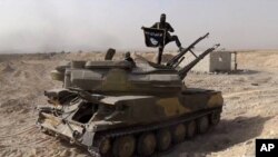 FILE - An Islamic State militant holds the group's flag as he stands on a tank captured from Syrian government forces, in the town of al-Qaryatayn southwest of Palmyra, central Syria. 