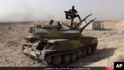 FILE - An Islamic State militant holds the group's flag as he stands on a tank captured from Syrian government forces, in the town of al-Qaryatayn southwest of Palmyra, central Syria, photo released on Aug. 5, 2015. 