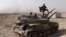 FILE - An Islamic State militant holds the group's flag as he stands on a tank captured from Syrian government forces, in the town of al-Qaryatayn southwest of Palmyra, central Syria. 