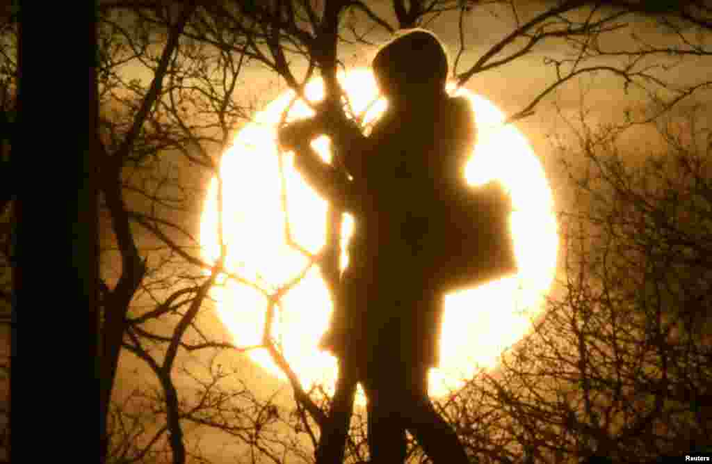 A woman takes photographs in front of the setting sun on Primrose Hill in London, Britain.