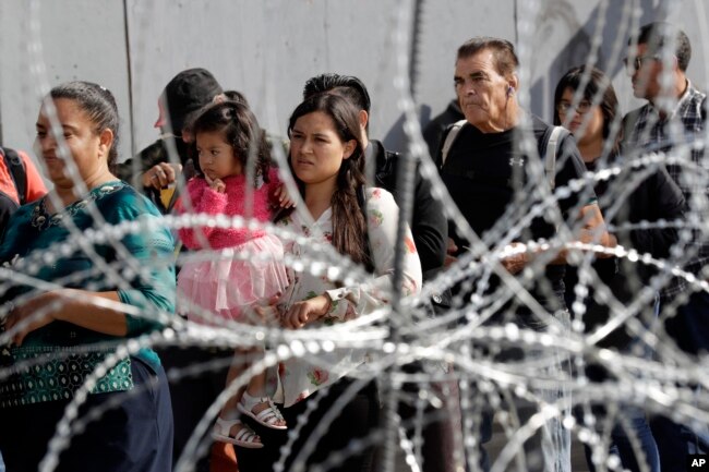 People line up to cross into the United States from Tijuana, Mexico, seen through barriers topped with concertina wire at the San Ysidro port of entry, Nov. 19, 2018, in San Diego.