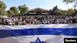 FILE —People gather in front of Israeli flag, as friends and family mourn Vivian Silver, 74, a Canadian-born peace activist from Kibbutz Beeri at a memorial service, at Kibbutz Gezer, Israel November 16, 2023.