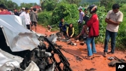 In this photo provided by Cambodia National Police, onlookers stand around the mangled wreckage of Cambodia's Prince Norodom Ranariddh's car after a collision with another vehicle outside Sihanoukville, Cambodia, Sunday, June 17, 2018. Ranariddh has been seriously injured in the road crash that killed his wife and injured at least seven other people early Sunday. (Cambodia National Police via AP)