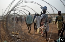 FILE - Displaced people walk next to a razor wire fence at the United Nations base in the capital Juba, South Sudan, Jan. 19, 2016.