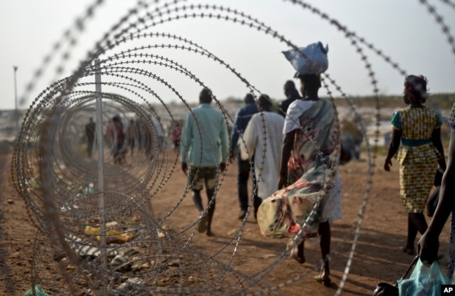 FILE - Displaced people walk next to a razor wire fence at the United Nations base in the capital Juba, South Sudan, Jan. 19, 2016.
