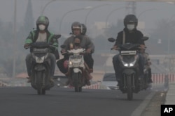 Riders wear mask as they pass through the haze from forest fires in Palembang, South Sumatra, Indonesia, Friday, Oct. 6, 2023. (AP Photo/Muhammad Hatta)