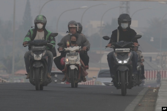 Riders wear mask as they pass through the haze from forest fires in Palembang, South Sumatra, Indonesia, Friday, Oct. 6, 2023. (AP Photo/Muhammad Hatta)