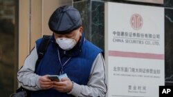 A man checks on his smartphone outside a stock brokerage that was closed except for limited transactions conducted through the glass of its front doors in Beijing, Wednesday, March 11, 2020.