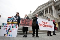 FILE - Protesters hold signs outside the U.S. Capitol, Jan 31, 2020, in Washington, as senators continue the impeachment trial of President Donald Trump.