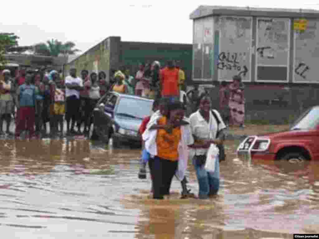 Pessoas tentando atravessar a estrada, numa Luanda inundada.