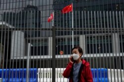 FILE - A woman wearing a protective face mask stands in front of a Chinese national flag and a Hong Kong flag outside government headquarters, in Hong Kong, February 4, 2020.