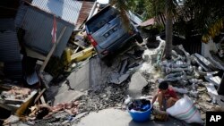 A boy sits with items salvaged from the ruins of a family member's house in the Balaroa neighborhood in Palu, Central Sulawesi, Indonesia Indonesia, Oct. 2, 2018. 