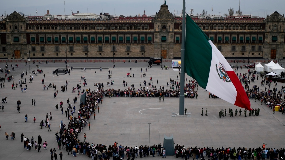 La gente observa la ceremonia de izamiento de la bandera en el Zócalo de la Ciudad de México, el sábado 20 de enero de 2024.