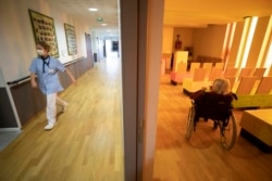 FILE - A nurse walks in a corridor of a nursing home as a resident sits in a chapel during COVID-19 testing in Bergheim, eastern France.