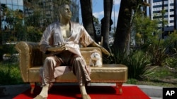 A dog named "Sassi" sits next to a golden statue of a bathrobe-clad Harvey Weinstein, seated atop a couch on the sidewalk along Hollywood Blvd., in Los Angeles Thursday, March 1, 2018. The piece, titled "Casting Couch," is a collaborative effort between a Los Angeles street artist known as Plastic Jesus and Joshua "Ginger" Monroe, creator of the nude Donald Trump statue. Plastic Jesus said the piece was meant to shine a light on the entertainment industry's sexual misconduct crisis and the disgraced movie mogul's prominent role in it. 