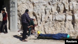 FILE - People stand near a dead body, after what rescue workers described as a gas attack in the town of Khan Sheikhoun in rebel-held Idlib, Syria, April 4, 2017.