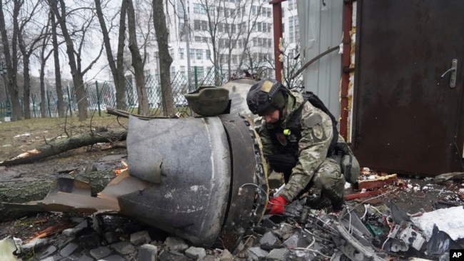 FILE - A Ukrainian police officer inspects a rocket part near a residential building damaged by a Russian missile strike in Kharkiv, Ukraine, Tuesday, Jan. 2, 2024.